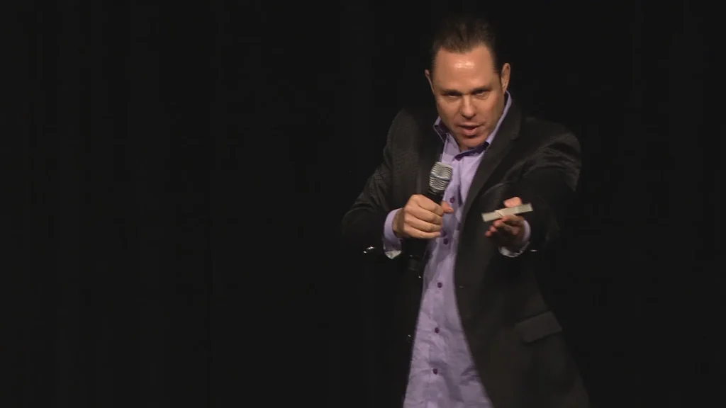 Randy Charach with holding mic and performing on stage.