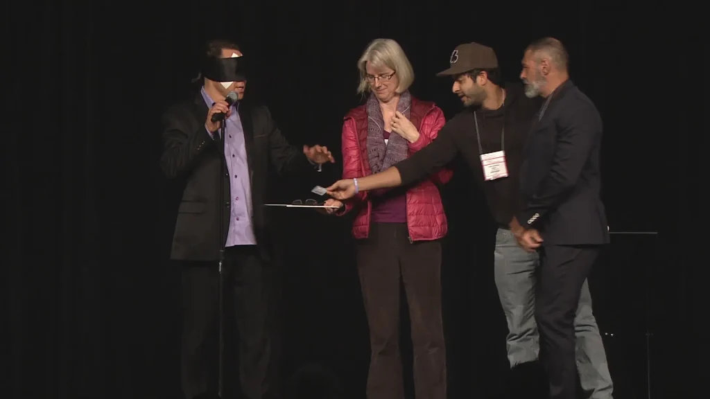 Randy Charach, blindfolded, and doing magic and mentalism act with audience participants.