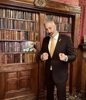 Ben Silver, with book shelve behind him, pointing finger towards the camera.