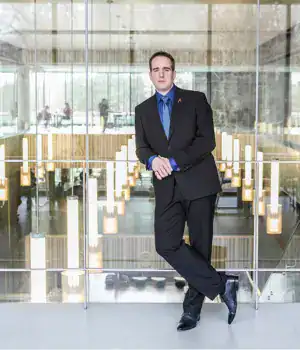 James, standing, wearing black pants and coat with a blue shirt.